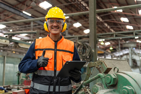 Confident engineer man with safety helmet standing analyzing with tablet in factory warehouse. Asian technician factory inspection and control machinery in industry factory.