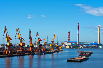 Obraz premium Industrial port with cranes barges and factory smokestacks under a clear blue sky