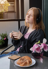 beautiful teenager girl in headphones with cup of tea on balcony