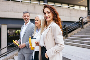 Group of businesspeople walking outside office, holding reusable coffee cups and water bottles