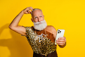 Photo of ancient aged caveman hold smart phone scratch head wear leopard skin clothes isolated on...