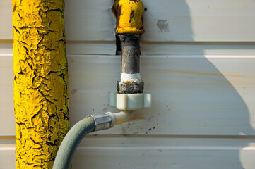 Brightly colored yellow gas pipe connects to a flexible hose against a textured wall, showcasing industrial details in natural light
