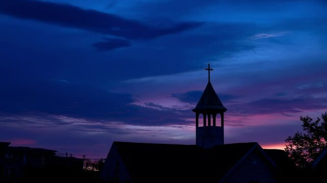 The fading colors of the sky create a beautiful contrast against the dark silhouette of the churchs belfry, with the bright, shining cross on top serving as a focal point and symbol