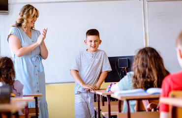 Smiling teacher assisting young boy with assignment at school.