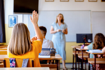 Rear view of girl raising hand to answer teacher's question during class in classroom.