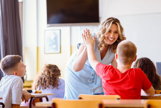 Smiling teacher assisting young boy with assignment at school desk in classroom.