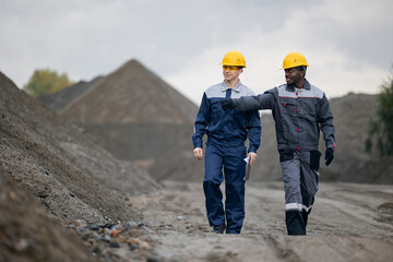Surveying engineers in sand quarry, two adult males, caucasian and african, discussing ore mining...