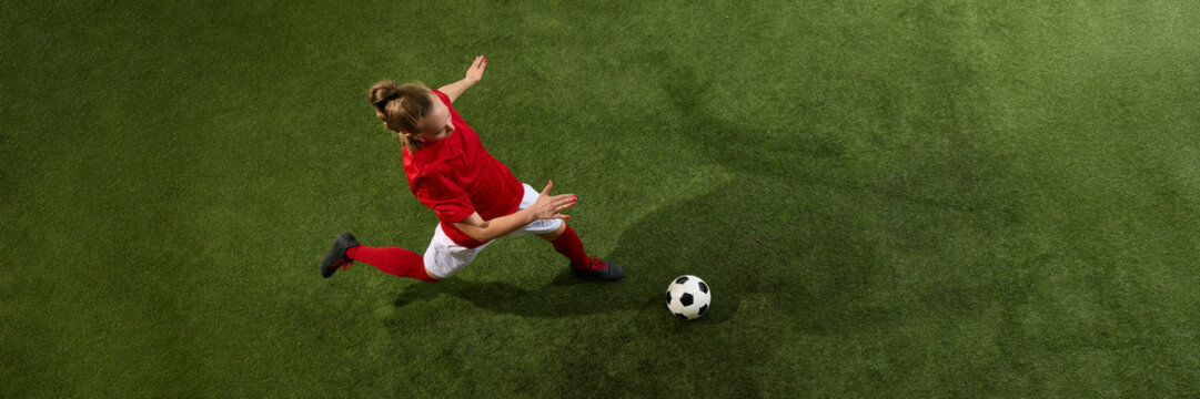 Fototapeta aerial view of female football player stretching to kick ball from above view with dynamic motion on green grassy playground with copy space. Banner. Concept of sport, strength, tournament, energy