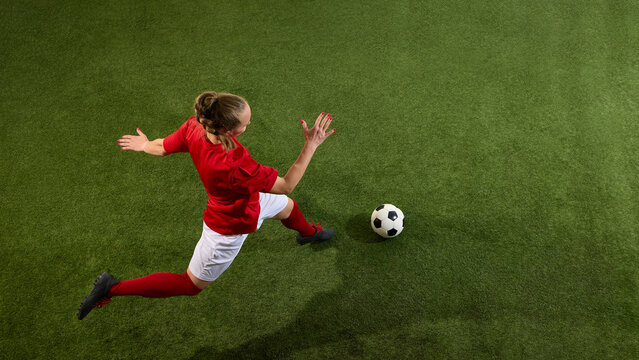Aerial view photo of athletic female footballer jumps wide in preparation for strong ball strike on green grassy playground. Concept of sport, youth, energy, power, action, competition - Powered by Adobe