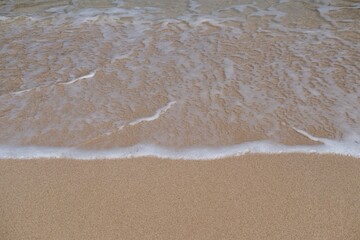 Close up wave on beach. Tide waves with bubbles foams running on sand. Beautiful seashore with beige sand and turquoise clear wave water sea