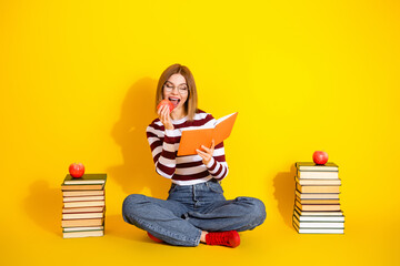 Young woman in a striped shirt enjoying reading with a red apple and book on a vivid yellow...