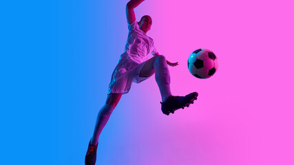 Female soccer player performs vertical jump with football in flight under striking pink-blue lights...