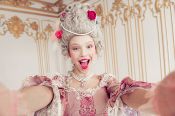 Young woman dressed in a regal baroque costume joyfully captures a selfie amidst ornately decorated...