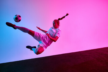 Dynamic photo. Young female footballer performing flying side kick in air with braided hair and...