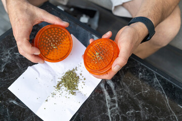 Grinding Cannabis With A Plastic Herb Grinder Over White Paper
