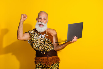 Photo of aged savage caveman raise fist hold laptop wear leopard skin outfit isolated on yellow...