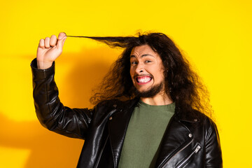 Handsome young man with long black hair wearing a leather jacket posing humorously against a bright yellow background
