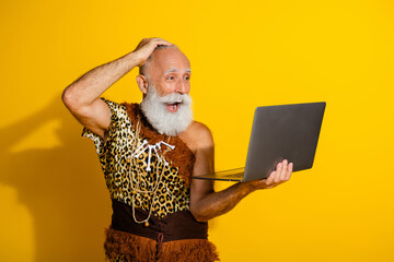 Photo of shocked barbarian guy dressed leopard fur holding modern device blank space isolated yellow color background