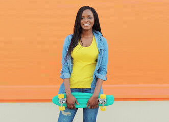 Summer portrait of stylish happy African young woman with skateboard, modern black teenage girl