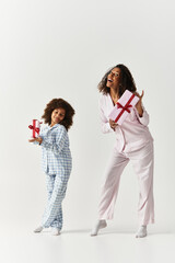Joyful mother and daughter with matching pyjamas hold gifts in studio