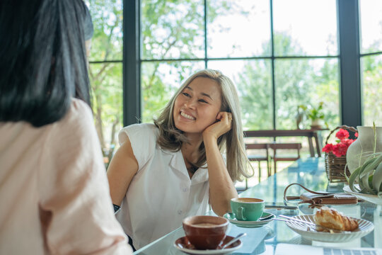 Two girl friends drinking coffee in the cafe. Two women at cafe, talking, laughing and enjoying their time. Lifestyle and friendship concepts with real people models. - Powered by Adobe