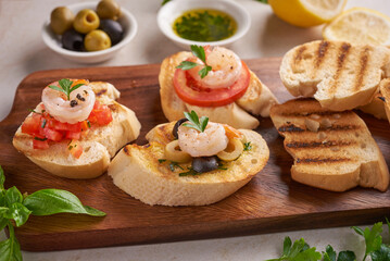 Olives, oil, Grilled shrimps and fresh vegetable salad on a wooden board on black slate stone board over dark background, juicy tomatoes on fresh bread, pesto as topping. top view. Flat lay