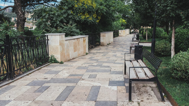 Quiet stone-paved park alley with benches, iron fence, and lush green trees urban nature concept