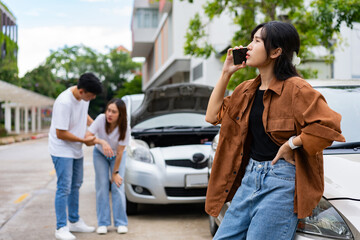 Asian Woman drivers call insurance after a car accident before taking pictures and sending insurance. Car Accident Emergency, while another person tends to a passenger with an injury.