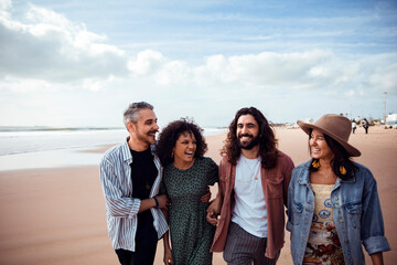 Group of four diverse friends laughing and walking on a sunny beach