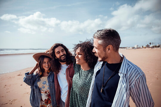 Group of four diverse friends laughing and walking on a sunny beach