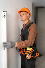 Measurement and house repair. Elderly builder or construction worker in protective hard hat checking level of wall.