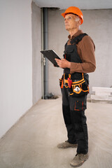 Elderly male builder in hardhat with clipboard builders at construction site. business, building and paperwork