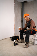 sad tired construction worker finishing work at home sits and drinking coffee.