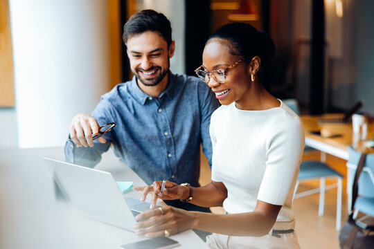 Two professionals at a desk using a laptop in a bright office setting - Powered by Adobe