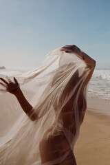 Covered in a sheer veil, the model turns away from the ocean, catching soft morning light. A...