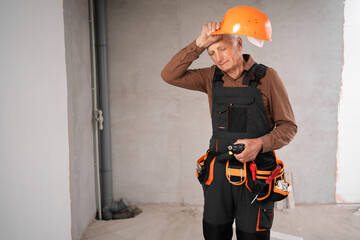 Senior builder man in uniform with hard hat standing in repairing house, tired frustration worker. Repair, house renovation and construction