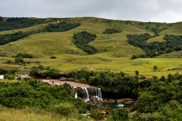 Cascading Mawsawa waterfall of Meghalaya and emerald pool in a grassy landscape.