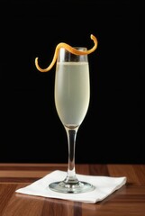 Champagne Cocktail: Elegant champagne cocktail in a coupe glass, garnished with an expressive orange peel twist. The drink rests on a crisp white napkin atop a rich, dark wood surface.