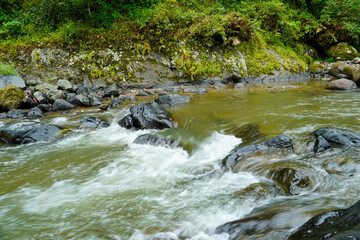 a moderately flowing river flowing past large rocks in the river with a cliff backdrop.