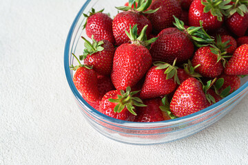 Fresh sweet strawberries in a glass bowl on a white background. Seasonal berries.