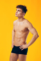 Fototapeta premium Athletic young man posing confidently against a vibrant yellow background, showcasing toned physique, reflecting strength and fitness.