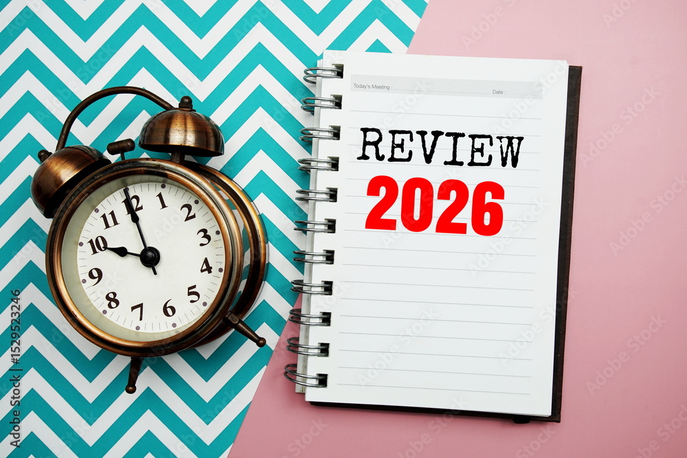 Poster review 2026 text on paper notebook with alarm clock top view on pink background