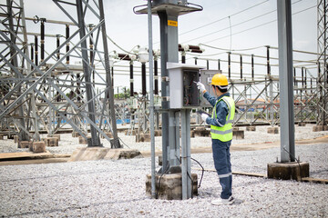 Fototapeta premium Engineer is working attentively at high voltage substation wearing safety gear and yellow helmet while inspecting electrical equipment in industrial outdoor environment
