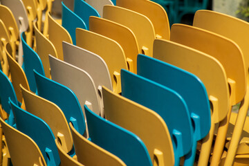 Naklejka premium Colorful rows of stacked plastic chairs in yellow, blue, and beige.