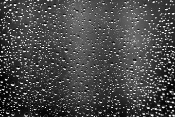 Monochrome texture of rain drops on window glass against city building background. Close-up