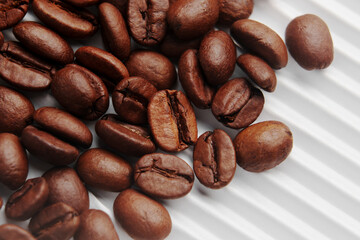 Roasted Arabica coffee beans scattered on white ribbed paper of store packaging. Macro. 