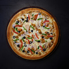Chicken pizza on a wooden board with some olive and vegies on it