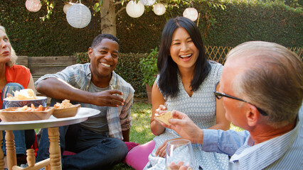Group Of Smiling Mature Friends Enjoying Drinks And Snacks In Backyard Garden Together