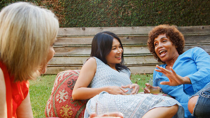 Group Of Smiling Mature Female Friends Enjoying Drinks And Snacks In Backyard Garden Together