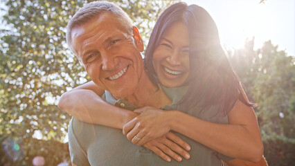 Outdoor Portrait Of Mature Couple With Woman Hugging Man From Behind With Lens Flare
